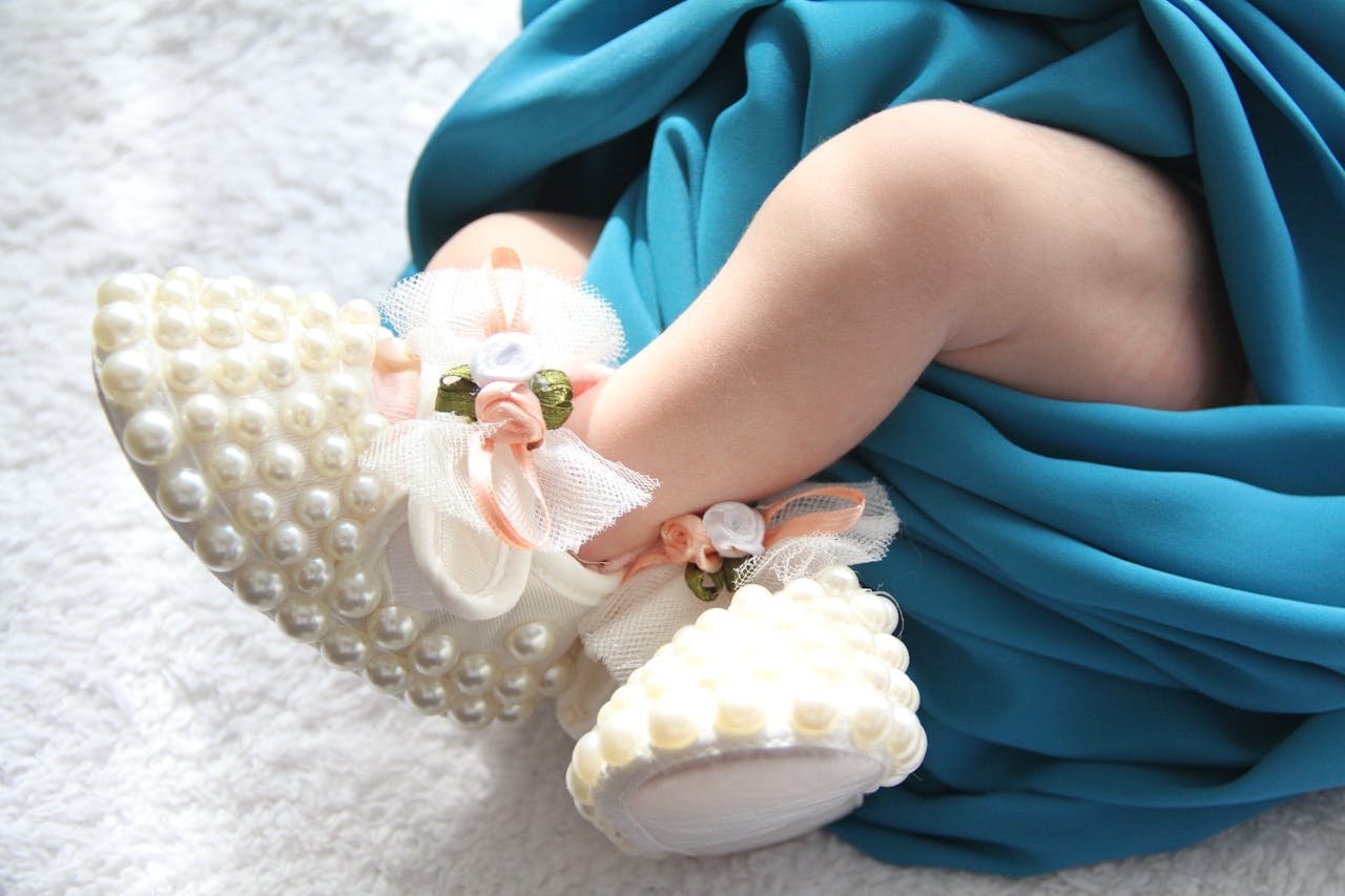 A baby in blue dress and pearls is laying on the floor